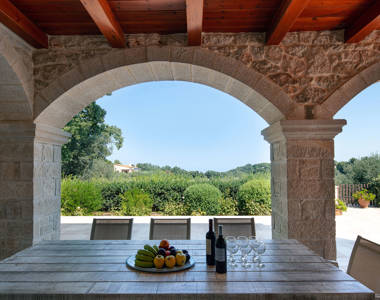 Vederi Estate Villa Melpomeni outdoor table with two bottles of wine, wine glasses and fruits and beautiful view