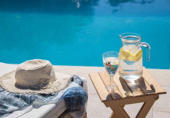 Vederi Estate Villa Melpomeni poolside small table with a jug and a glass of water with lemon slices in them